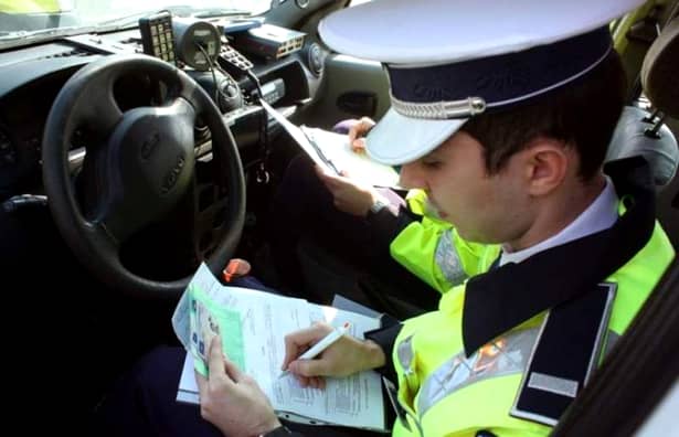 Noi schimbări aduse Codului Rutier. Un poliţist scrie o amendă în maşina sa