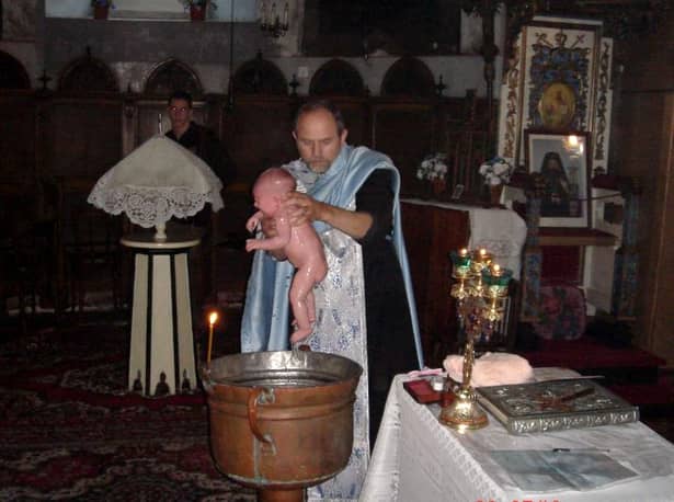 Un copil primeşte taina botezului în Biserică, de la preot