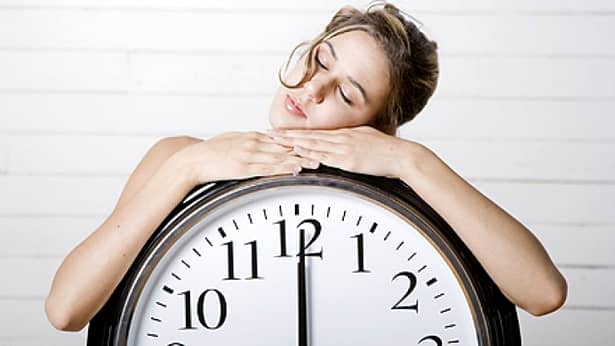 Femeie care doarme pe un ceas care arata ora 12 fix