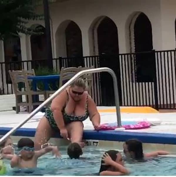 Femeia care se rade pe picioare în piscina hotelului este îmbrăcată în costum de baie și poartă ochelari de soare la ochi.